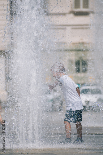 Fototapeta Naklejka Na Ścianę i Meble -  Kid or child playing with water near a fountain during hot summer day, vertical