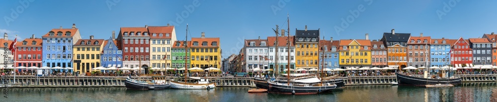 Panorama view of Nyhawn, the colorful houses next to the old port. Tourist visiting restaurants, cafes and ships in the canal. The most important sightseeing spot in Copenhagen, Denmark. - obrazy, fototapety, plakaty 