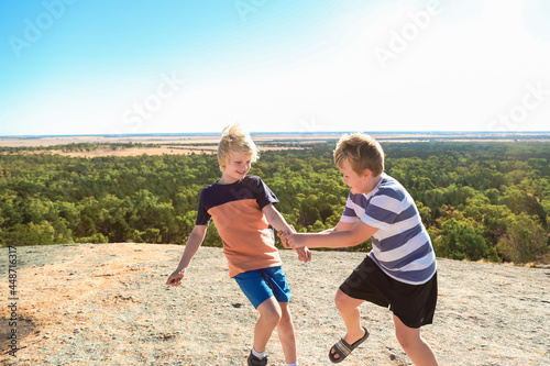Two boys exploring hill top on large rock formation in the Terrick Terrick National Park, Victoria Australia