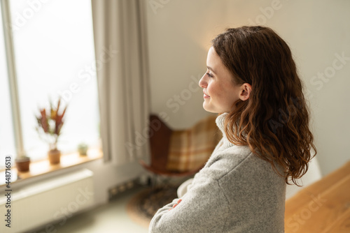 Young woman gazing out of a window with a smile