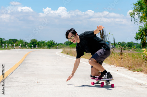 A young Asian man is wearing a black shirt and pants. play skateboard Show the posture of a turn around. On a country road on a sunny day with sky. Looking at the camera, Play surf skate. © Ekkasit A Siam