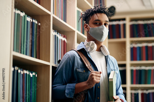 Photo Portrait of black male student wearing protective face mask in library and looking at camera
