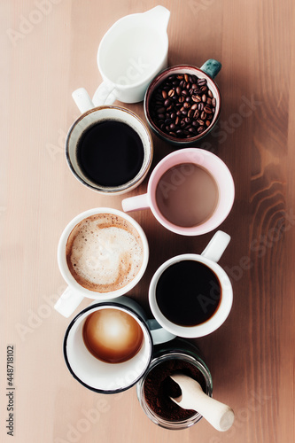 Multiple coffee cups, milk, beans and ground coffee in jar on wooden background