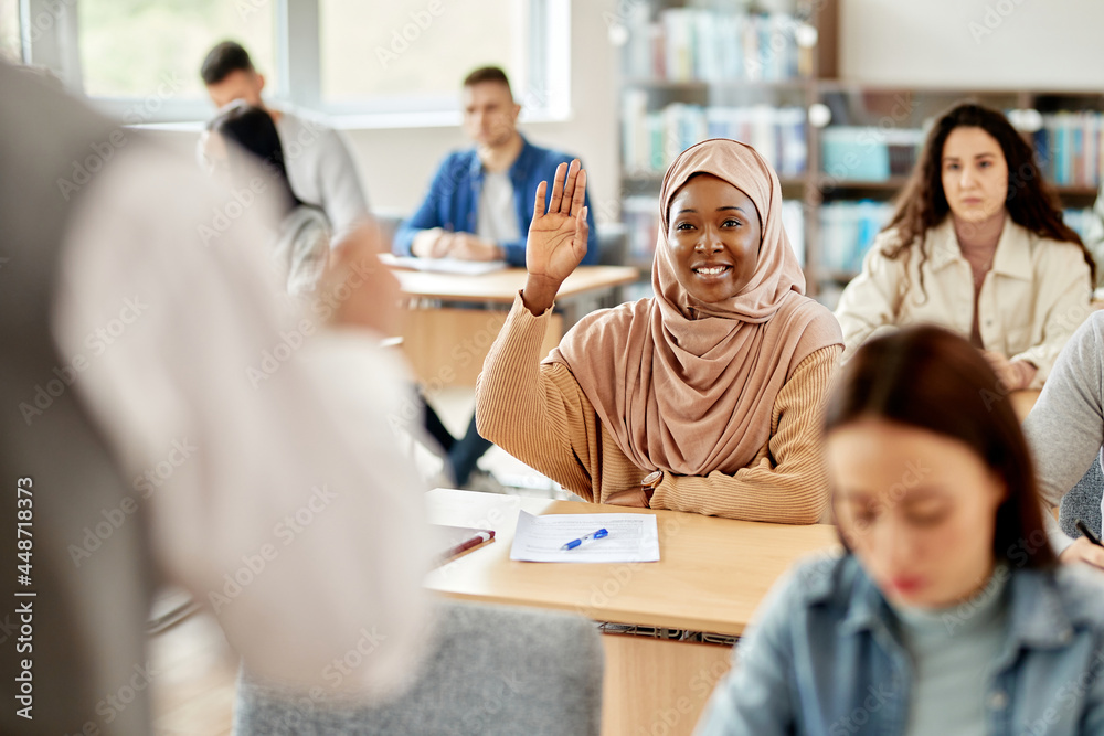Happy African American student in hijab raising her had to ask a question during lecture at the university. Happy African American student in hijab raising her had to ask a question during lecture at the university.