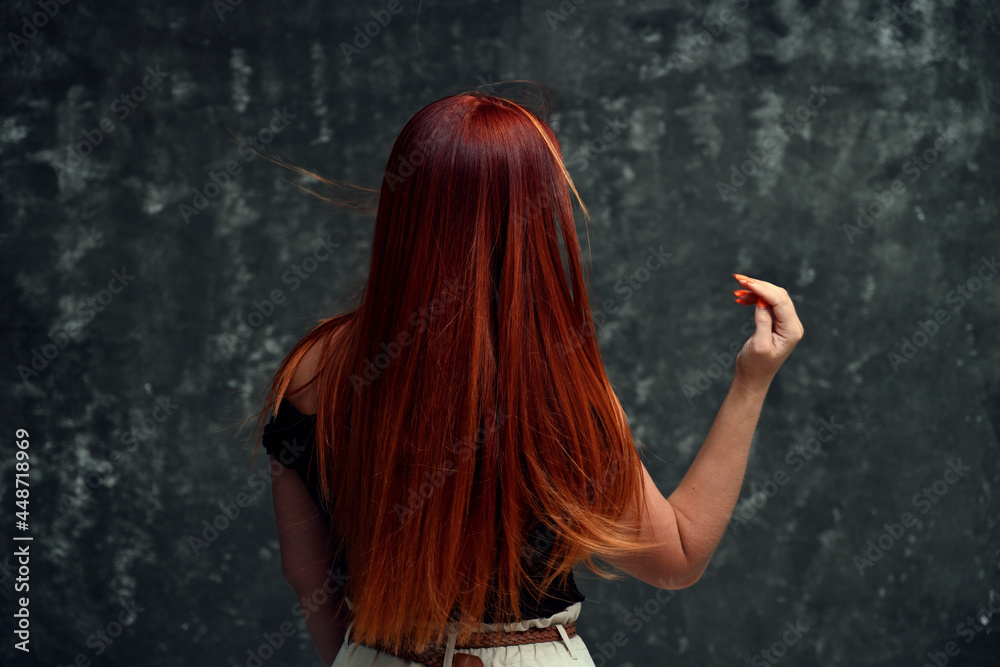 Obraz premium Red-haired Caucasian girl model with long curly hair on a gray background. Back view