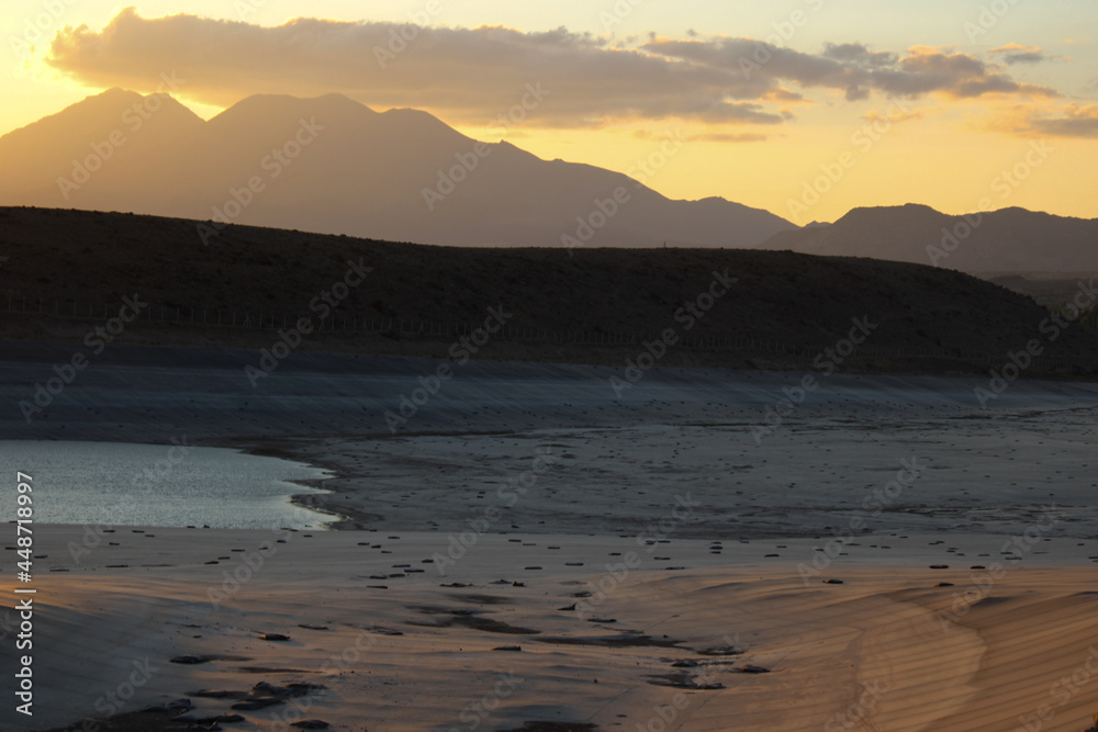 Fototapeta premium Dried lake on summer. Water crisis and drought impact case or climate change. Low tide lake. Withdrawal of dam water as a result of global warming. Declining water dams and lake. Sunset. Cloudy sky