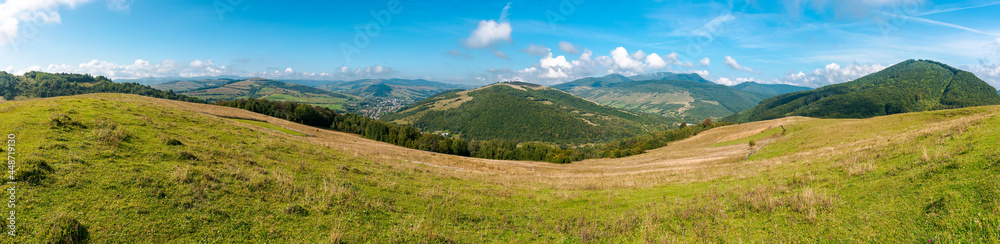 Obraz premium carpathian countryside in september. beautiful mountain landscape with grassy field on the hill. rural scenery with village in the distant valley on a sunny day with clouds on the sky