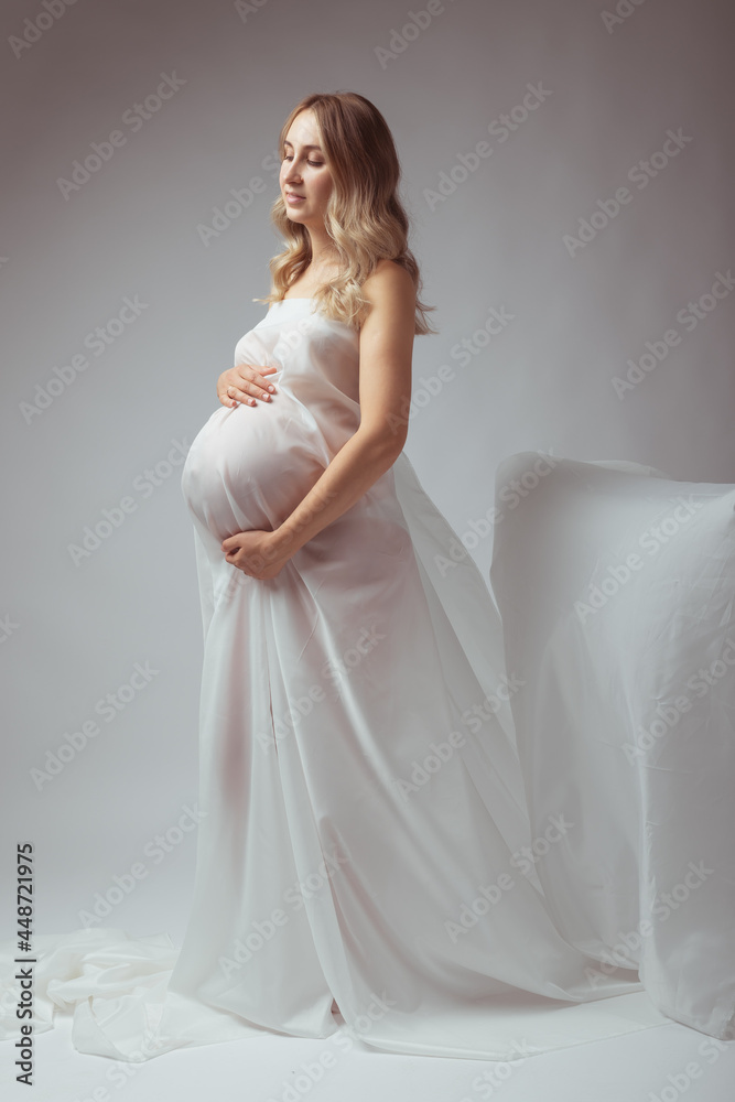 Pregnant woman in white long dress on light background Pregnant woman in white long dress on light background