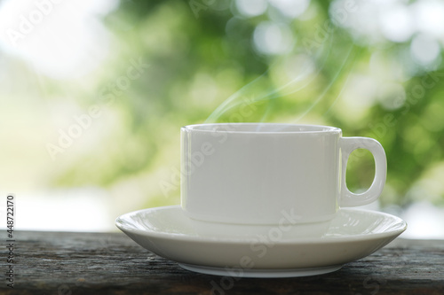 Close-up front view of a cup of tea Coffee with white saucers on a wooden table laid out in a green garden with morning sunlight gives a soothing feeling to start the day.