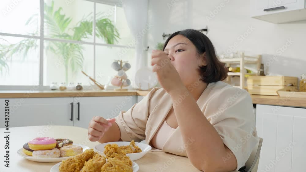 Asian young oversize big women eat unhealthy foods in kitchen at home. Asian young oversize big women eat unhealthy foods in kitchen at home.