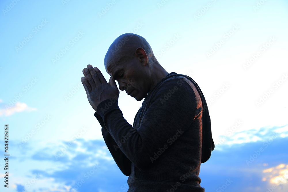 black man praying to god Caribbean man praying with blue sky in the background stock photo