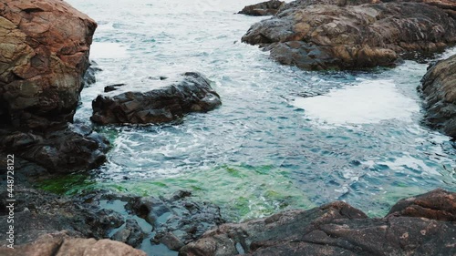 Gentle blue sea waves rushing and splashing between dark cliffs forming white foam and revealing green seaweed