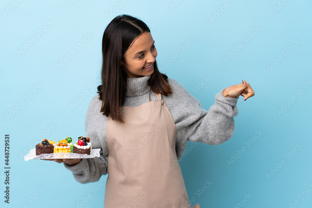 Pastry chef holding a big cake over isolated blue background giving a thumbs up gesture. Pastry chef holding a big cake over isolated blue background giving a thumbs up gesture.