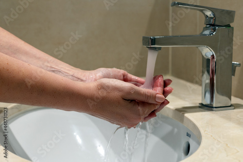 Water flow to woman`s hand from water tap or faucet in a bathroom