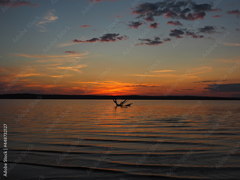 Summer sunset on the Kama river. Driftwood in the water. Beautiful clouds. Russia, Ural, Perm Territory, Elovo. Summer sunset on the Kama river. Driftwood in the water. Beautiful clouds. Russia, Ural, Perm Territory, Elovo.