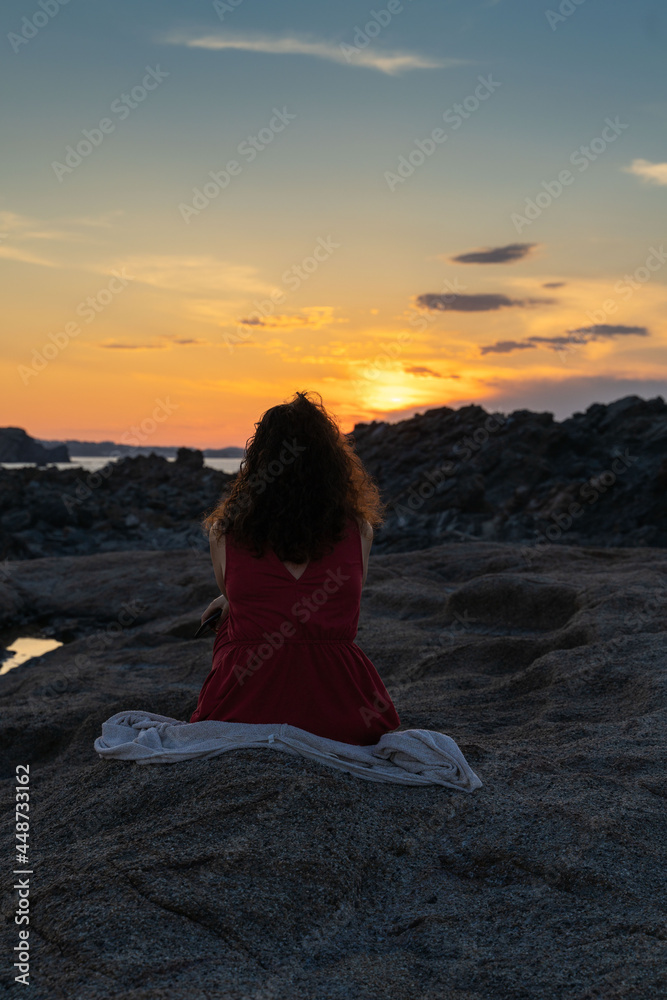 woman sitting on the beach, contemplates the sunset
