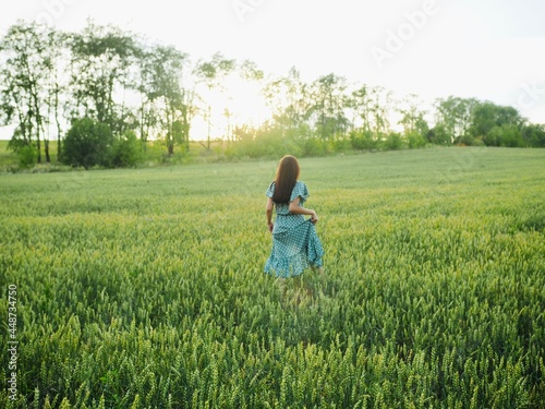 Happy woman in dress running in sunlight on summer field, enjoying life. Girl brunette long black hair fly in wind. Nature beauty, blue sky, field wheat. Freedom, Sustainable lifestyle, Wellness