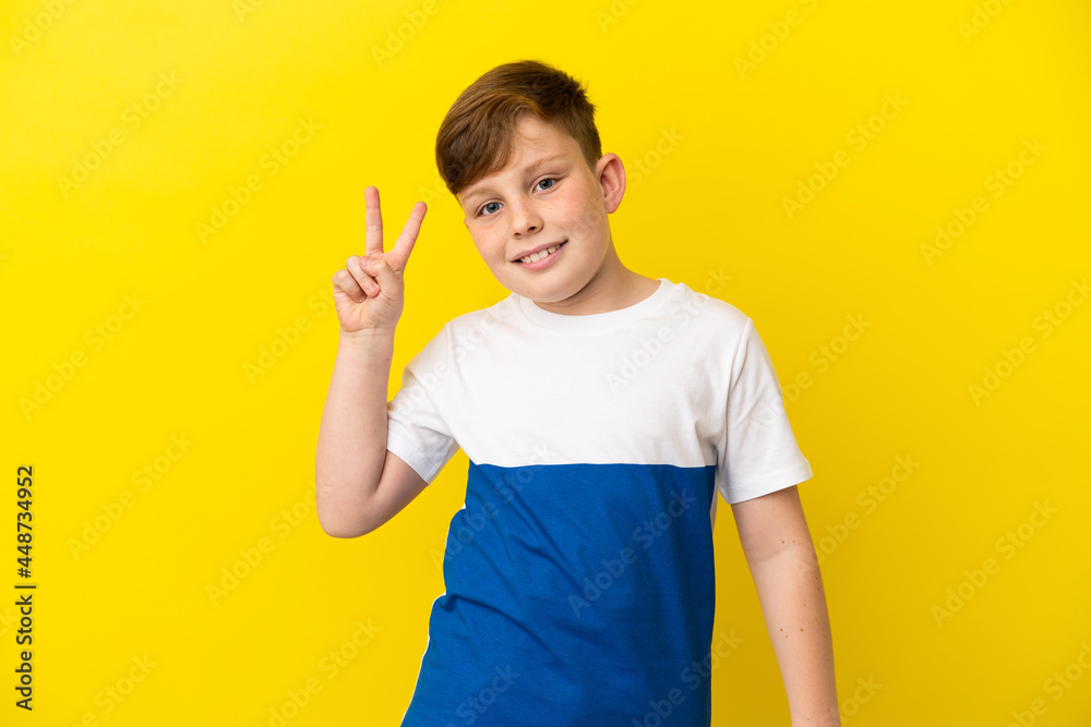 Little redhead boy isolated on yellow background smiling and showing victory sign Little redhead boy isolated on yellow background smiling and showing victory sign