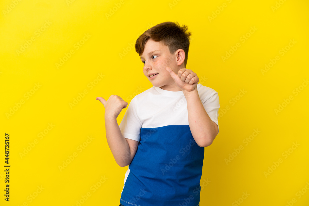Little redhead boy isolated on yellow background pointing to the side to present a product Little redhead boy isolated on yellow background pointing to the side to present a product