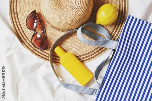 Flat lay photography beach essentials. Straw hat, stylish brown sunglasses, sunscreen cream, lemon and bag in white and blue stripes. Top view summer travel photo