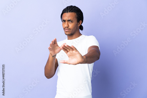 Young African American man with braids man isolated on purple background nervous stretching hands to the front