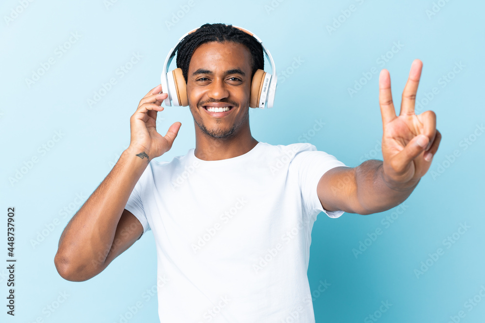 Naklejka premium Young African American man with braids isolated on blue background listening music and singing