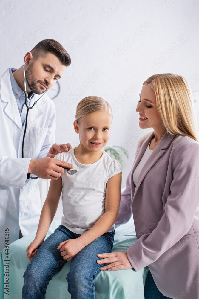 Smiling kid looking at camera near mom and doctor with stethoscope Smiling kid looking at camera near mom and doctor with stethoscope