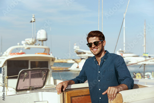 Pleased young man on board of his yacht in harbor