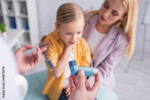 Doctor holding inhaler near sick kid and mother on blurred background