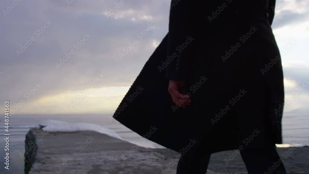 A lonely young man walking on pier to the iced lake. Back rear view of man dressed a black coat . Shot on RED EPIC-W 8K Helium Cinema Camera in Slow Motion.
