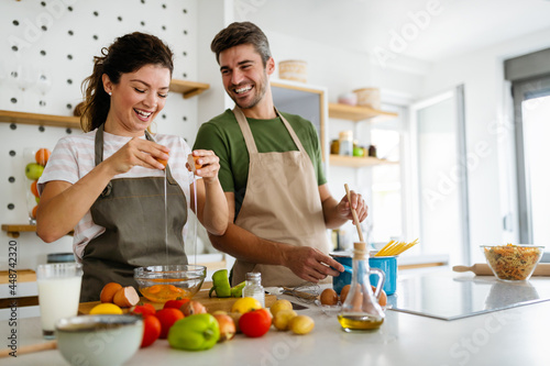Obraz na plátně Young happy couple is enjoying and preparing healthy meal in their kitchen