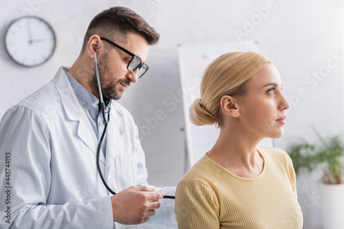 doctor in white coat and eyeglasses examining blonde woman with stethoscope