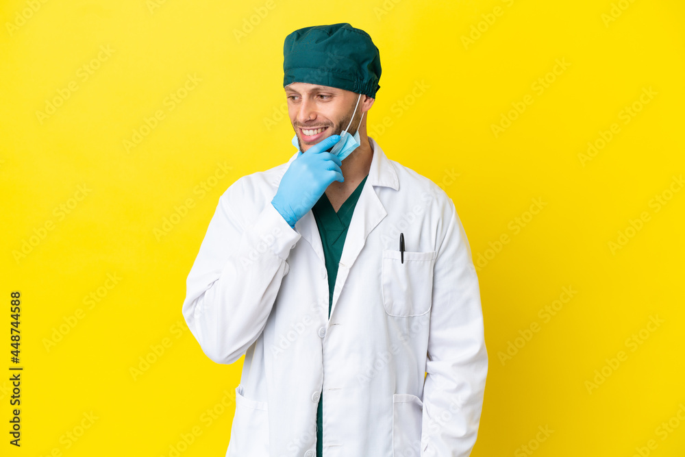 Surgeon blonde man in green uniform isolated on yellow background looking to the side Surgeon blonde man in green uniform isolated on yellow background looking to the side