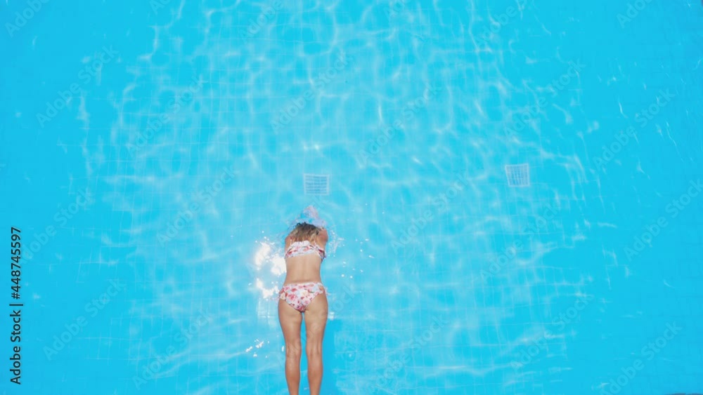 Girl dived into the water - pool. Top view of jumping into the pool in slow motion. Woman swims underwater.