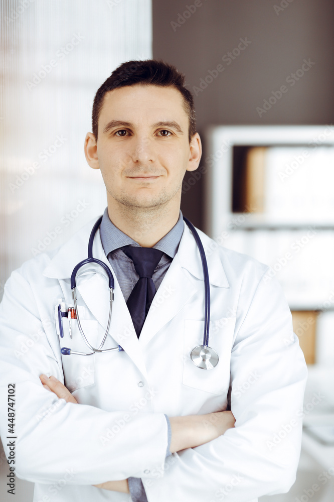 Male doctor standing straight in sunny clinic. Perfect medical service in hospital Male doctor standing straight in sunny clinic. Perfect medical service in hospital