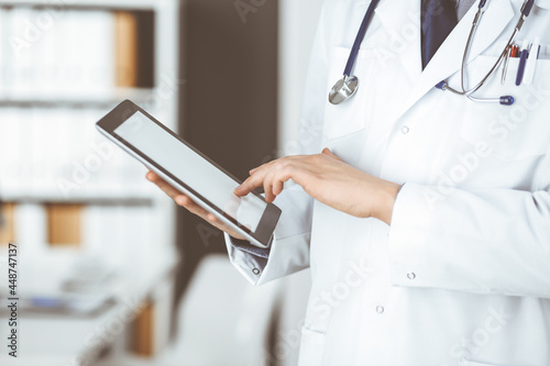 Unknown male doctor using tablet computer in clinic near his working place, closeup. Perfect medical service in hospital. Medicine and healthcare concept