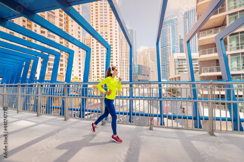 Photography Young woman in bright sportswear quickly runs across a pedestrian bridge in the Dubai Marina district