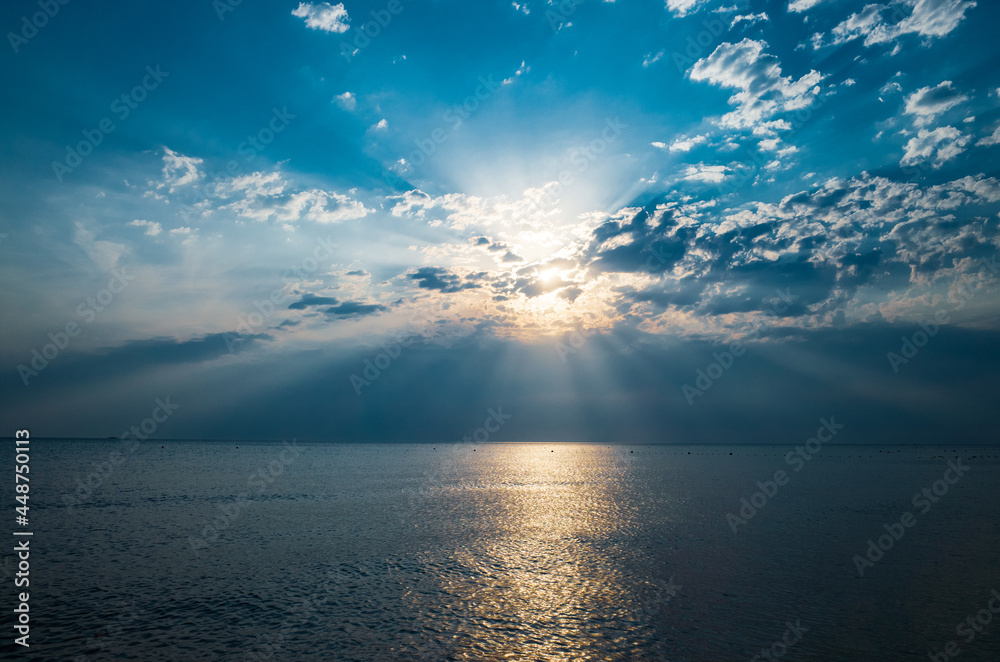 Fototapeta premium God rays in the seascape. Sun rays shine through the clouds at sunrise, sea background. Copy space.