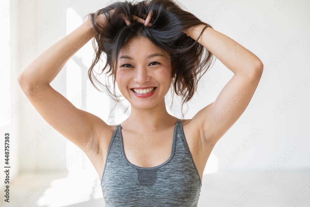 Fototapeta premium Young beautiful Asian girl smiles and plays with her hair. She is wearing a sporty top and red lipstick
