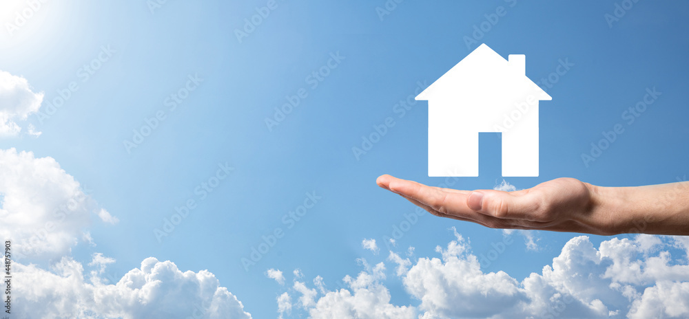 Naklejka premium Male hand holding house icon on blue background. Property insurance and security concept.Real estate concept.Banner with copy space.