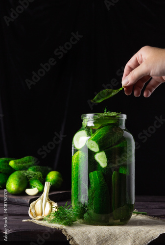 Pickling cucumbers. Cucumbers in a jar, the hand puts the ingredients. Vintage, dark background.