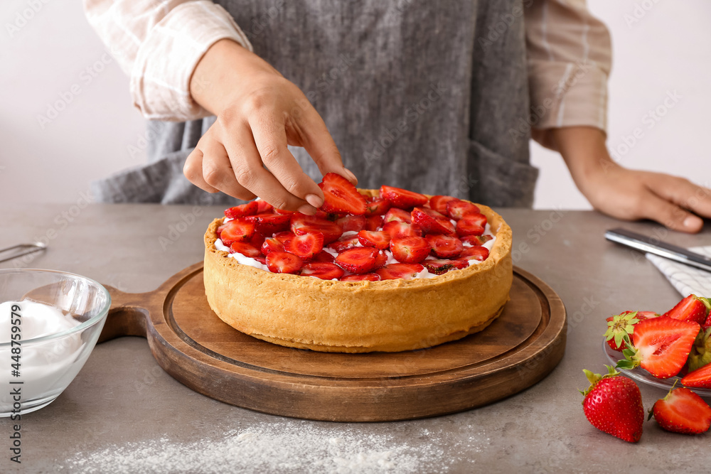 Woman decorating tasty pie with strawberry at table in kitchen, closeup Woman decorating tasty pie with strawberry at table in kitchen, closeup