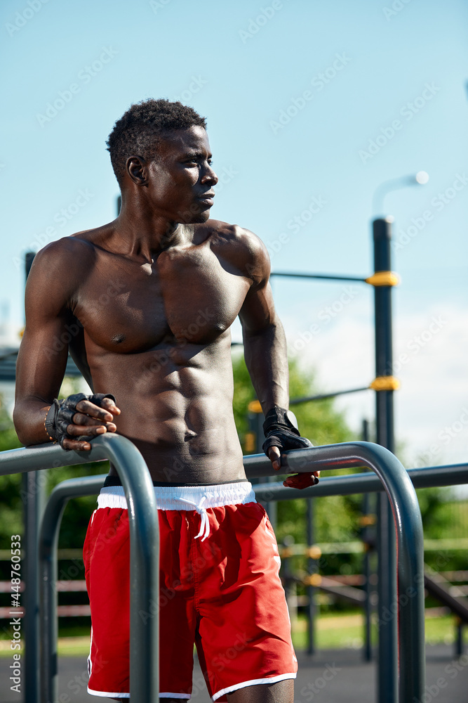 Black fitness man exercising dips, cross training of male model in urban environment. An African guy in his twenties is training on the street.