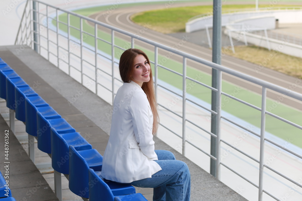 Fair-haired woman in white shirt and blue jeans at a stadium