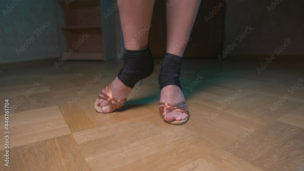 Legs of a slender Caucasian woman in ballroom shoes and a black latino workout dress. Basic movements in a dark room. Home dance workout Legs of a slender Caucasian woman in ballroom shoes and a black latino workout dress. Basic movements in a dark room. Home dance workout