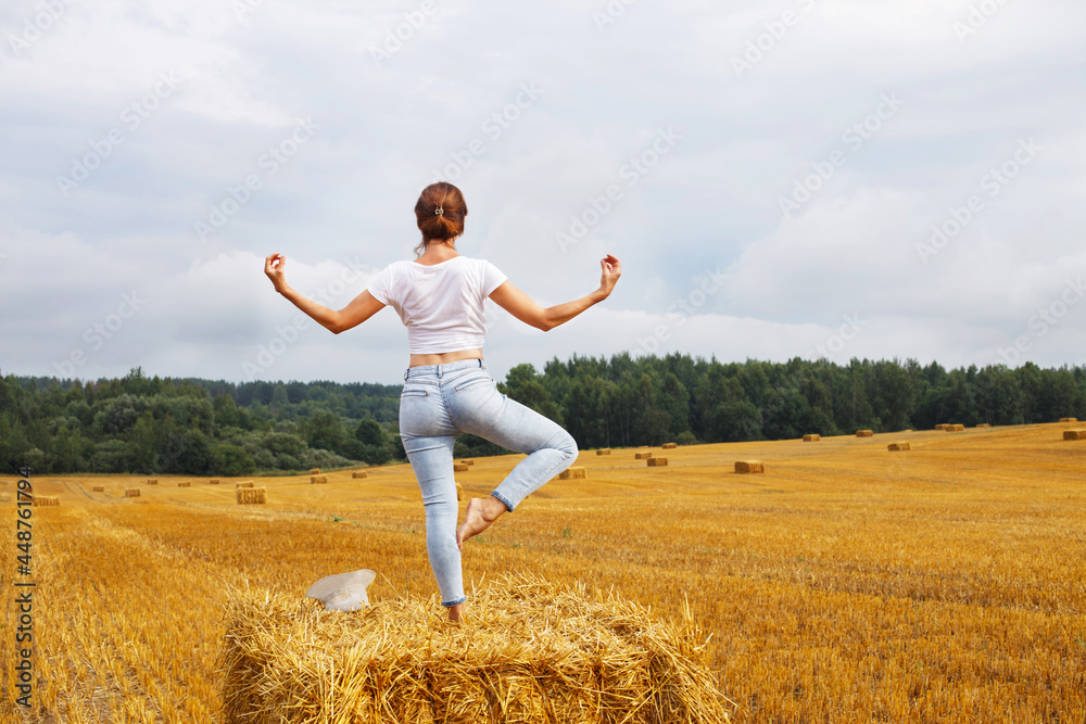 girl with straw hat stands on a haystack on a bale in the agricultural field after harvesting girl with straw hat stands on a haystack on a bale in the agricultural field after harvesting