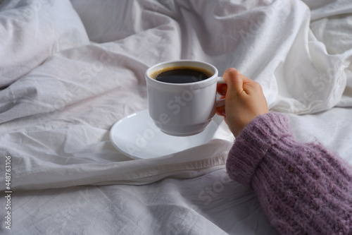 Girl holding a cup of coffee in bed. Breakfast in bed. Interior. Cosiness.