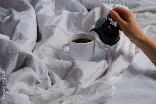The girl pours milk into a cup of coffee. Breakfast in bed. Interior. Cosiness.