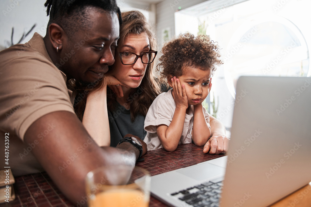 Girl feeling shocked while watching something at the laptop with her diverse parents Girl feeling shocked while watching something at the laptop with her diverse parents