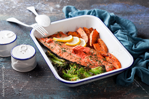 Baked sockeye salmon fish fillet with roasted sweet potato and broccoli, in enameled baking dish, selective focus photo